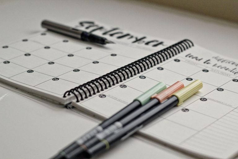 Calendar planning A spiral-bound planner with pens on a table, displaying a monthly calendar layout.
