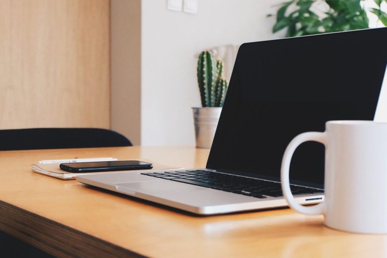 From Chaos to Admin Clarity A laptop, smartphone, and mug on a clean wooden desk with plants in the background.